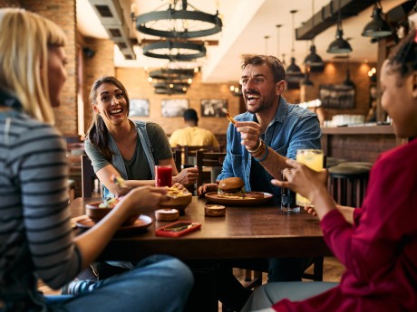 Young happy man communicating with is female friends while eating in a tavern.
